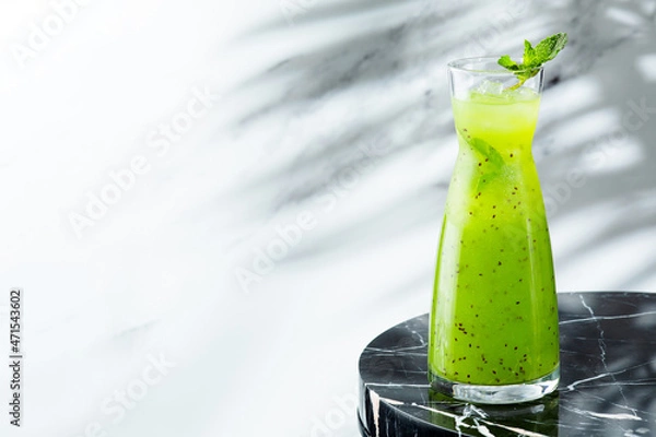Fototapeta green summer lemonade in jug on light background with shadow of branch tropic plant. Lemonade with kiwi and ice