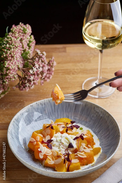 Fototapeta pumpkin with stracciatella and microgreen on wooden table. Woman hold fork with pumpkin and glass of white wine on background
