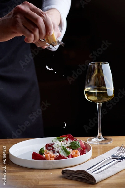 Fototapeta The chef prepares a salad with salmon. Rubs cheese on a grater. salmon salad with beet cheese and green leaves on wooden table with glass of white wine.