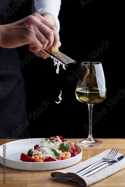 Fototapeta The chef prepares a salad with salmon. Rubs cheese on a grater. salmon salad with beet cheese and green leaves on wooden table with glass of white wine.