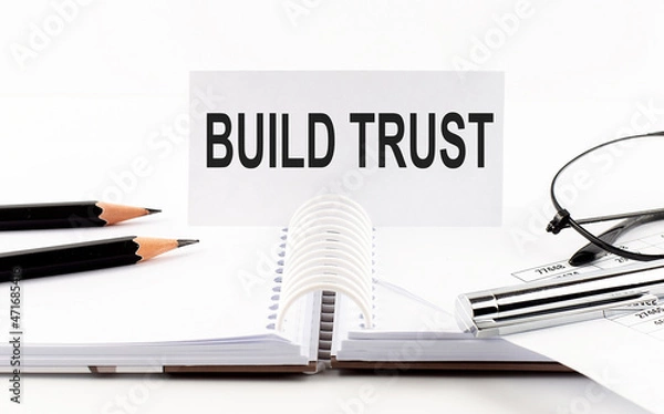 Fototapeta Text BUILD TRUST on paper card,pen, pencils, glasses,financial documentation on table - business concept