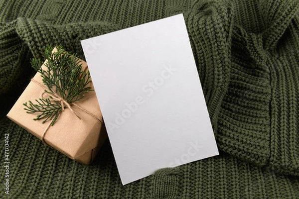 Obraz empty 5x7 card mockup kraft gift box with fir decoration on knitted green sweater, design element for wedding invitation, thank you or greeting card. Christmas winter card mock up background