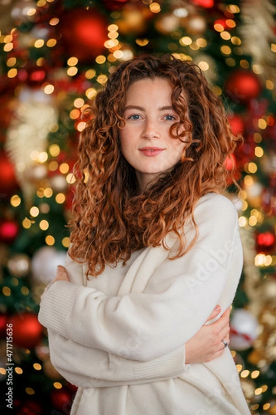 Obraz A beautiful red-haired girl portrait in a Christmas interior. Christmas theme. Cozy atmosphere. Christmas tree, decorated fireplace, lots of gifts, 
