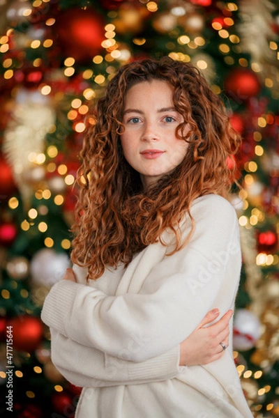 Obraz A beautiful red-haired girl portrait in a Christmas interior. Christmas theme. Cozy atmosphere. Christmas tree, decorated fireplace, lots of gifts, 