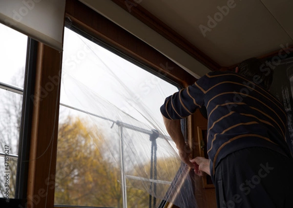 Obraz Pour combattre le froid, la condensation, et les différences intempestives de température, application d'un film transparent en plastique qui va remplacer le double vitrage traditionnel en verre