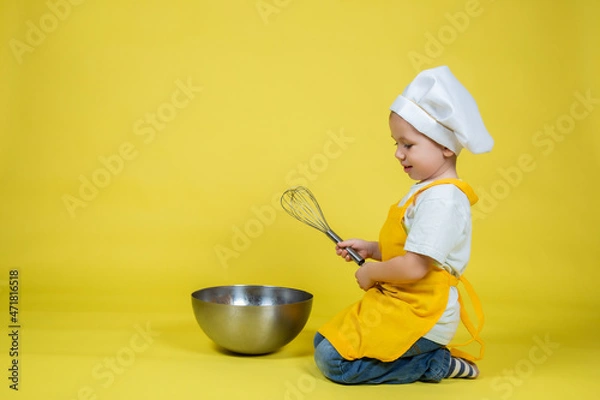 Fototapeta Boy in apron and chef's hat sitting on the floor with a bowl and whisk