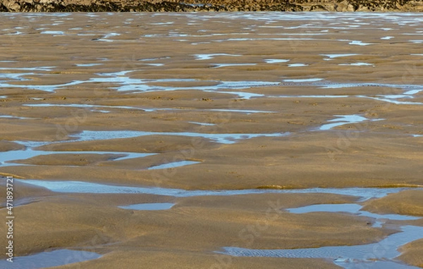Fototapeta Abstract image of an intertidal sandy beach after an ebb tide. with saltwater pools and sand formations caused by receding waters. Reflections of blue sky in the standing puddles. Landscape, Bude, UK.