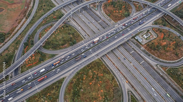 Fototapeta Top down aerial view from drone on modern traffic junction of multiple lane highway road in metropolis city. Heavy traffic on motorways. Elevated curved roads, clover shape bridge with no speed limit.