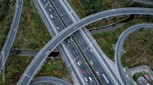 Fototapeta Top down aerial view from drone on modern traffic junction of multiple lane highway road in metropolis city. Heavy traffic on motorways. Elevated curved roads, clover shape bridge with no speed limit.