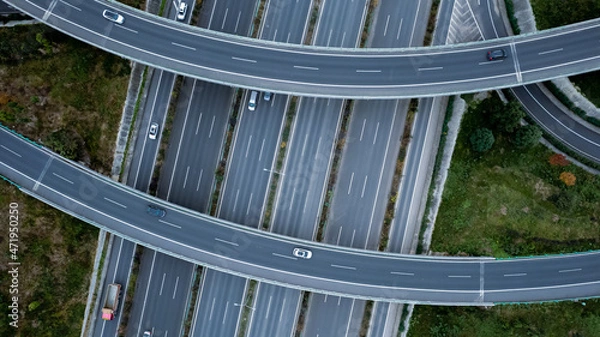 Fototapeta Top down aerial view from drone on modern traffic junction of multiple lane highway road in metropolis city. Heavy traffic on motorways. Elevated curved roads, clover shape bridge with no speed limit.
