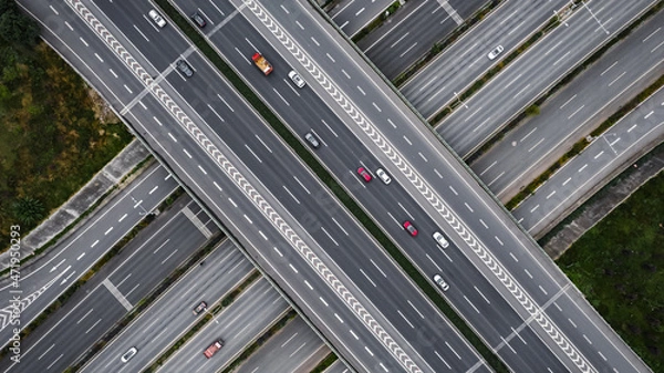 Fototapeta Top down aerial view from drone on modern traffic junction of multiple lane highway road in metropolis city. Heavy traffic on motorways. Elevated curved roads, clover shape bridge with no speed limit.