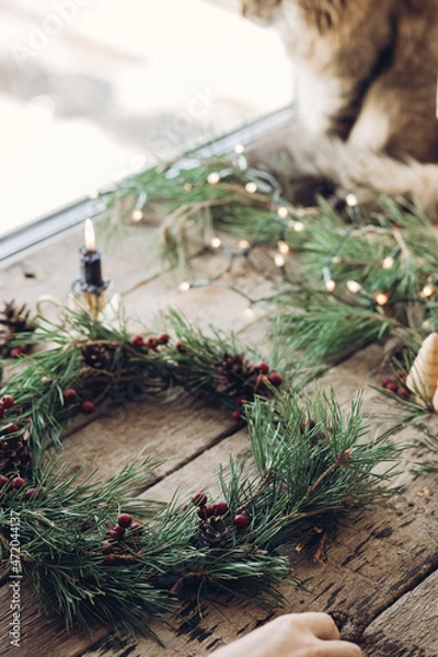 Obraz Woman making Christmas wreath by attaching red berries to fir tree branch during Christmas workshop, Handmade advent wreath creation process concept