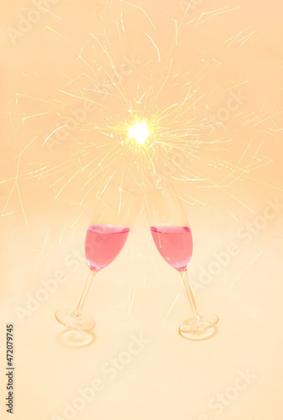 Fototapeta Christmas party concept with champagne glasses with rose pink wine toasting with sparklers behind on pastel peach background.  Winter holidays and New Year eve idea. Luxury aesthetic.