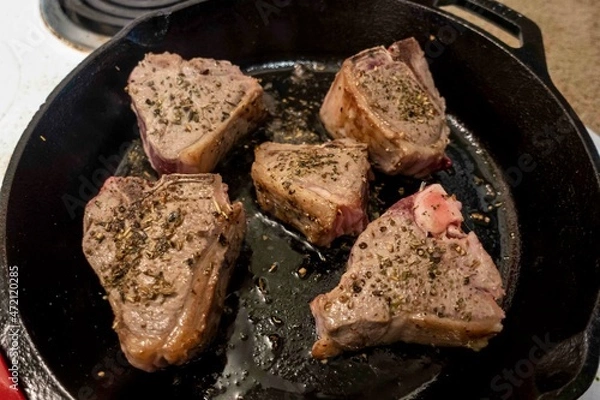 Fototapeta Close up view of several juicy lamb chops sizzling in a hot cast iron skillet on a white stove top