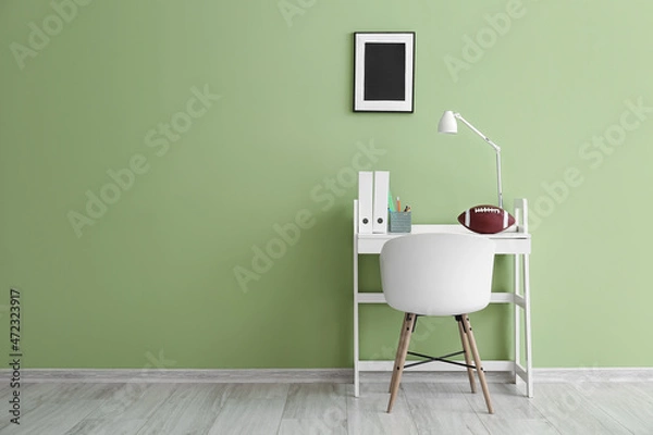 Fototapeta Modern workplace with folders and rugby ball near green wall