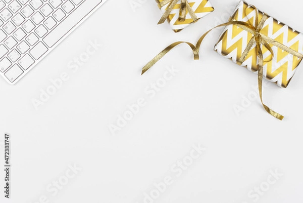 Fototapeta Christmas presents wrapped in golden paper with geometric print, keyboard on white background. Business concept. Freelancer work desk. Minimal festive composition. Birthday or anniversary gifts.