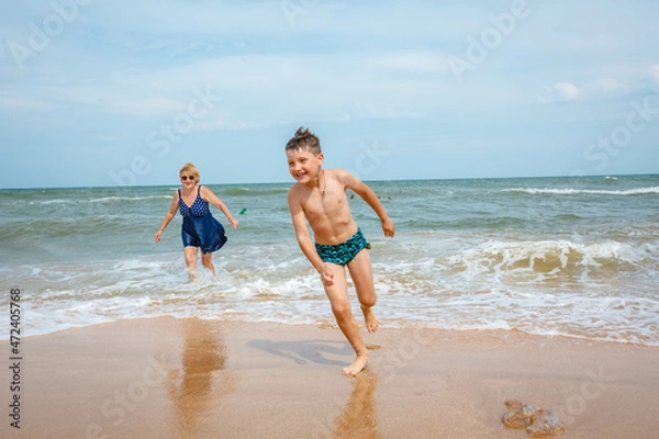Obraz A grandmother is playing with her grandson on the beach when the wave crashes on their feet.