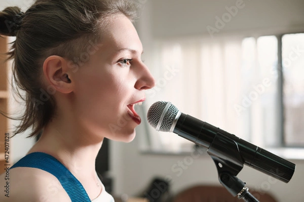 Fototapeta young emotional woman singing into a microphone. female rock singer on a rehearsal in record studio. side view