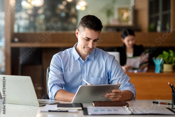 Fototapeta Charming businessman smiling using tablet work at the office.