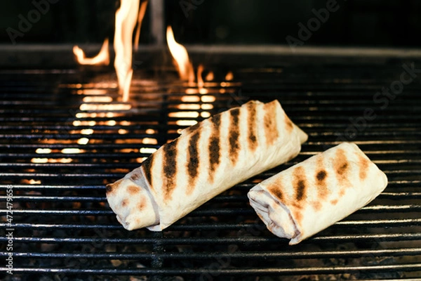 Fototapeta Shawarma with meat kebabs, on charcoal, on a fire, on a grill wire rack, with sauce, tomatoes, pepper, cheese, herbs, cabbage, onion and garlic in a ruddy pita bread, dark background