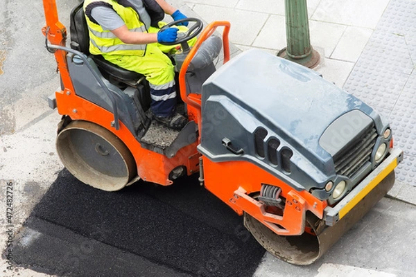 Fototapeta construction worker with small steamroller for repairing potholes and paving the road in city street
