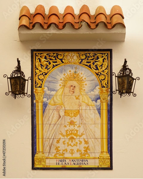Obraz Die allerheiligste Maria in Trauer gemalt auf Kacheln, die eine Außenwand einer Kirche in Algeciras schmückt. Von oben geschützt durch einen Baldachin und links und rechts beleuchtet durch 2 Laternen