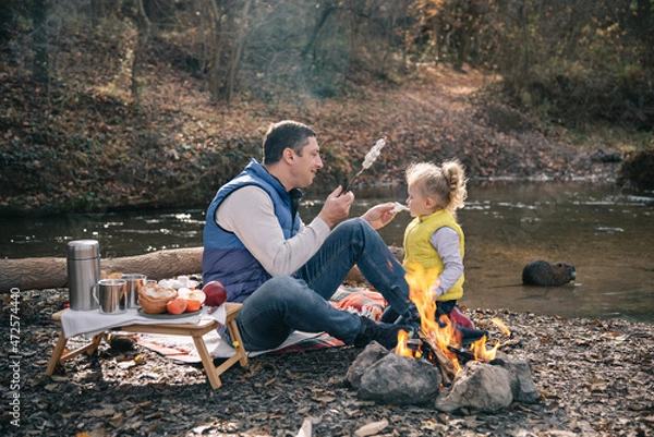 Fototapeta Dad and daughter fries marshmallows on sticks by the fire.