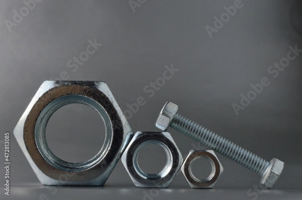 Fototapeta composition of new bolts and nuts of different sizes on a gray background.