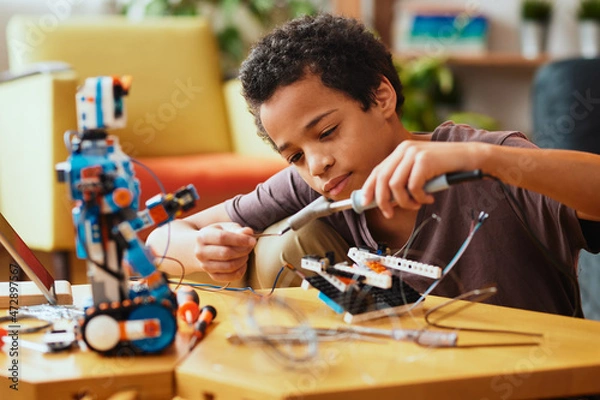 Obraz Smart African boy making a robot at home for science class. Robotics and education.
