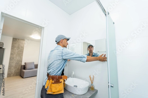 Obraz Handyman installing mirror in bathroom.
