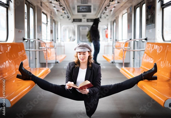 Fototapeta flexible female yogi reading book in the underground carriage sitting in gymnastic split. Concept of inspiration, harmony and health.