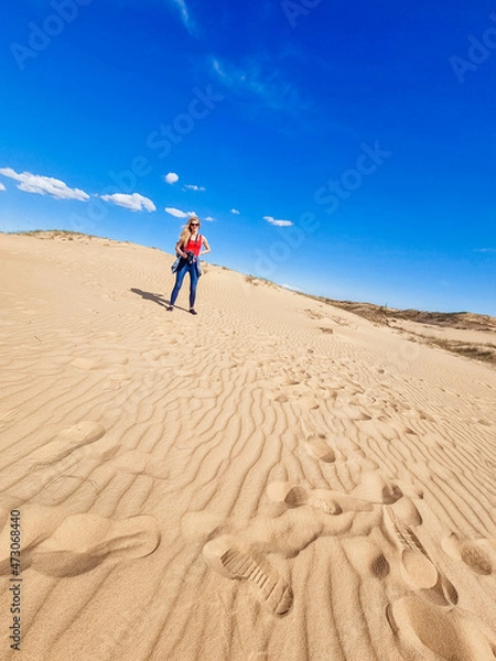 Fototapeta Young photographer stands with camera in Oleshky Sand, Ukraine. Standing on the top of sand dune in desert, sand is al around and some greens. Hot summer weather, concept of travelling around planet.