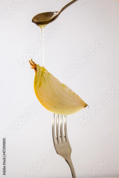 Fototapeta Onion with honey on a fork, close-up. On white background. Creative