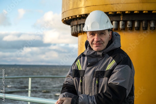 Fototapeta A professional in overalls. Shift worker of the Arctic oil platform. On his head is the white helmet of the master.