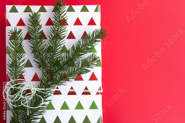 Obraz gift in beautiful package with a coniferous twig on a red background. Flat lay, copy space 