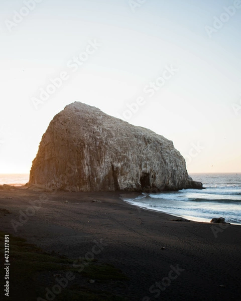 Fototapeta A big and beautiful rock church in the ocean, at sunset, with a beautiful light coming from it's back, in Constitución, Chile