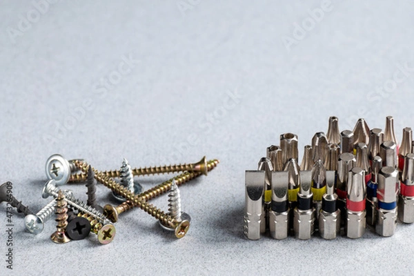 Fototapeta Screwdriver bits, electric screwdriver bits, different versions and various fasteners - screws, bolts, self-tapping screws on a grey background. Copy space.