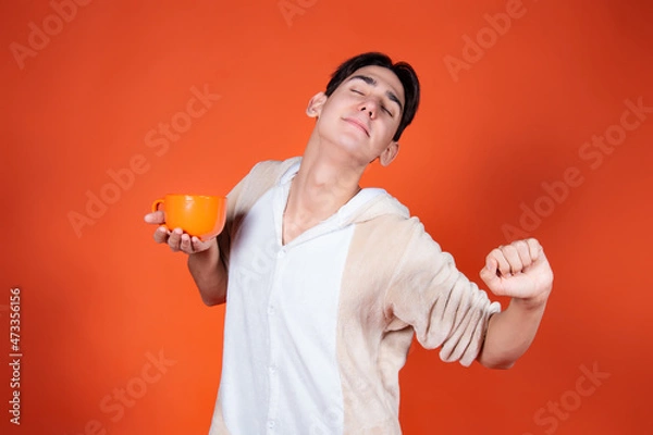 Fototapeta Cheerful man in pajamas with a mug of coffee on an orange background.