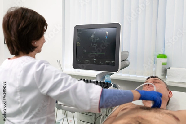 Fototapeta Woman doctor makes heart check of patient man using modern equipment in a cardiology clinic. Female cardiologist is screaning patient heart with ultrasonography, looking at screen. Healthcare concept