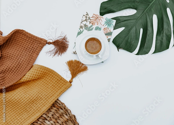 Obraz Coffee cup, Two blankets, craft note, and monstera leaf on white background, minimal simple background. Workspace flat lay