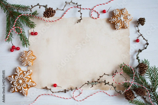 Fototapeta Christmas white wooden background with old paper for congratulation text, list, letter to Santa and fir branches, gingerbread cookies snowflakes, cones, red berries, red and white rope.