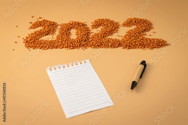 Obraz The number 2022 next to a notebook and a planning pen. The figure is made of bright orange shiny beads. Signs and symbols of the new year for copy space. Festive mockup.