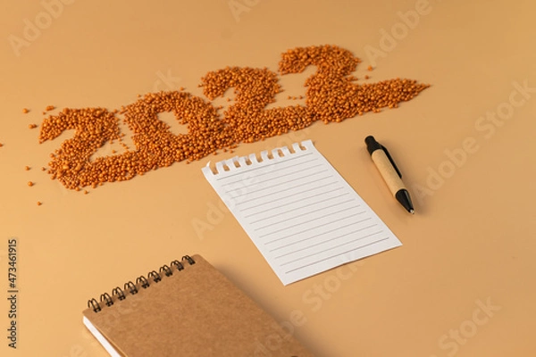 Obraz The number 2022 next to a notebook and a planning pen. The figure is made of bright orange shiny beads. Signs and symbols of the new year for copy space. Festive mockup.
