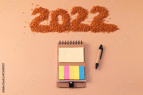 Obraz The number 2022 next to a notebook and a planning pen. The figure is made of bright orange shiny beads. Signs and symbols of the new year for copy space. Festive mockup.