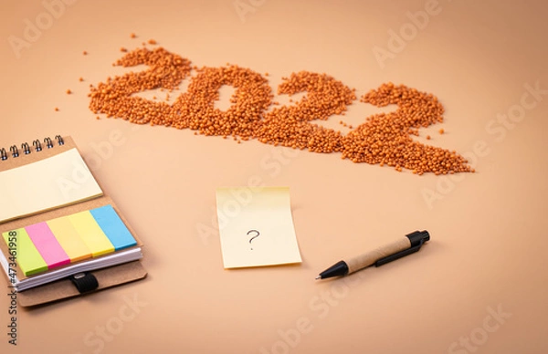 Obraz Number 2022, notepad, pen and sheet of paper with a question mark. The figurine is made of bright orange shiny beads. Signs and symbols of the new year for copy space. Festive mockup.