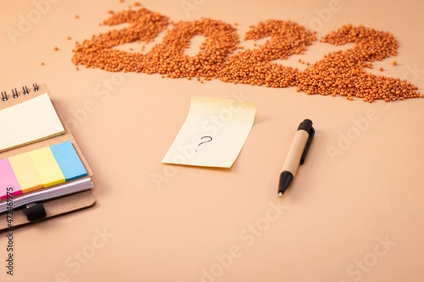 Obraz Number 2022, notepad, pen and sheet of paper with a question mark. The figurine is made of bright orange shiny beads. Signs and symbols of the new year for copy space. Festive mockup.