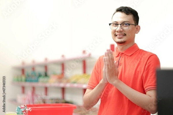Obraz Smiling young man cashier with a welcome greeting hand gesture