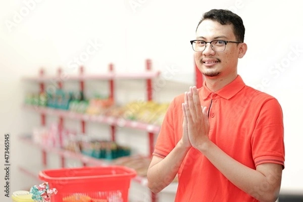 Obraz Smiling young man cashier with a welcome greeting hand gesture