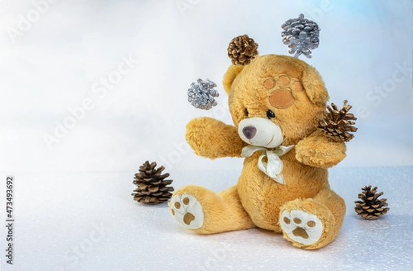 Fototapeta A teddy bear juggles New Year's cones on a light blue background. Selective focus