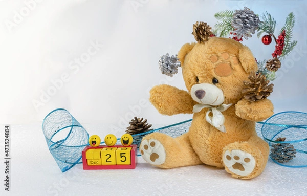 Fototapeta Christmas composition: a teddy bear juggles pine cones, a festive blue lace ribbon with sequins, a voluminous toy calendar with funny faces on the background of a New Year's wreath. Selective focus